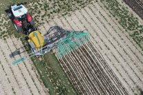 Das Foto zeigt einen roten Traktor mit gelbem Güllefass mit Schleppschlauch bei der Gärrestausbringung von oben.