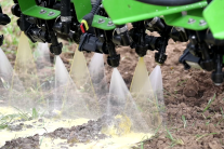 Düsen eines landwirtschaftlichen Anbaugerätes verteilen weißen und gelben Spritzstrahl auf Acker